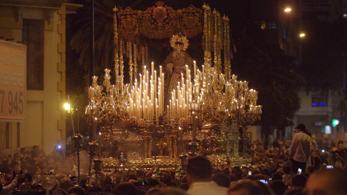 Nighttime procession in Málaga with the throne illuminated by candles among the crowd